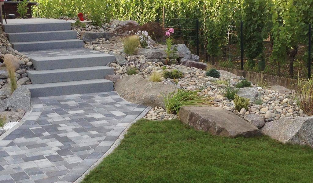 Aménagement d'un escalier extérieur sur une allée dallée en pierre à gauche d'un enrochement et d'une pose de gazon naturel