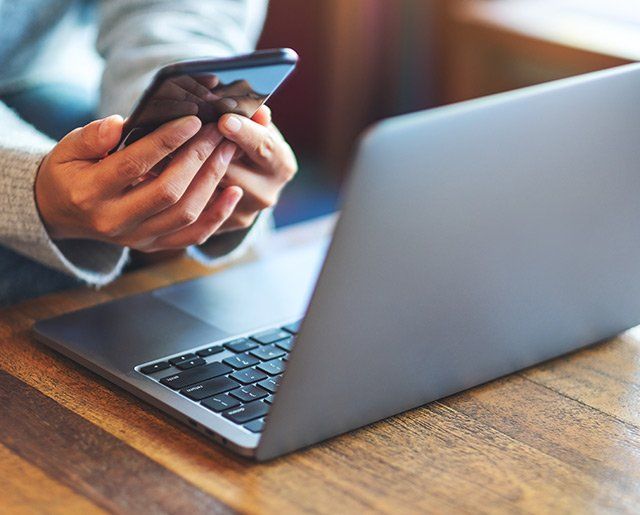 Femme utilisant un téléphonne portable façe à un ordinateur
