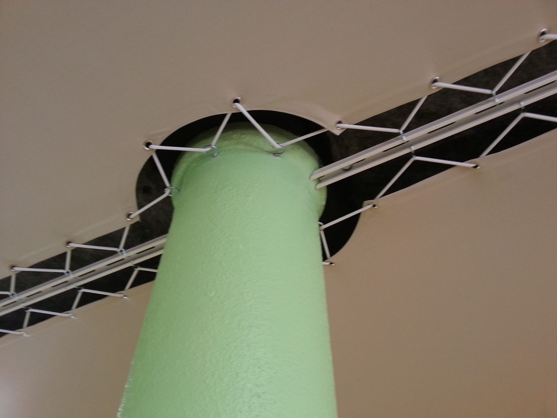 Un pilier vert émerge d'un plafond beige. Des supports métalliques noirs traversent le plafond, fixés par des attaches blanches.