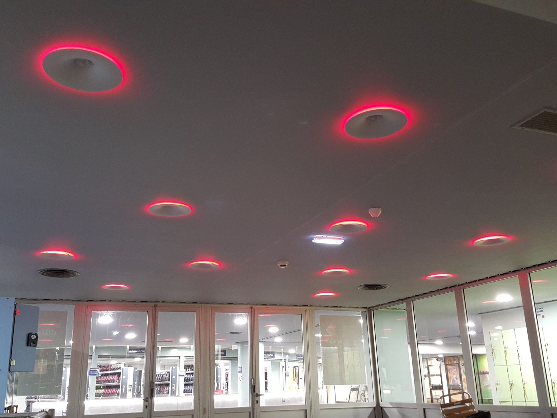 Plafond avec de nombreuses lumières en halos rouges, au-dessus d'une pièce avec des fenêtres et des portes en verre.