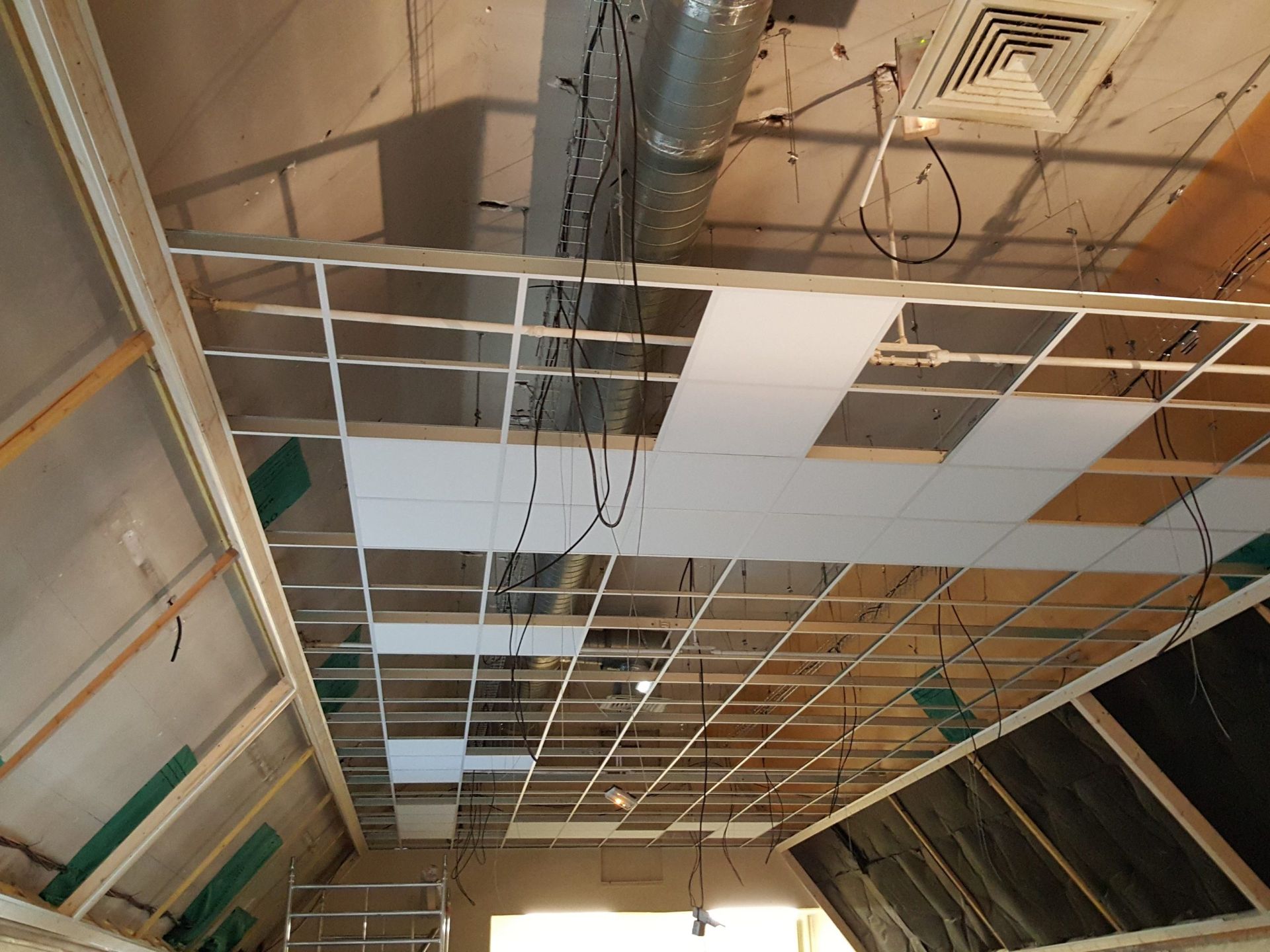 Construction : grille de plafond avec panneaux blancs partiellement installés, conduits et fils apparents.