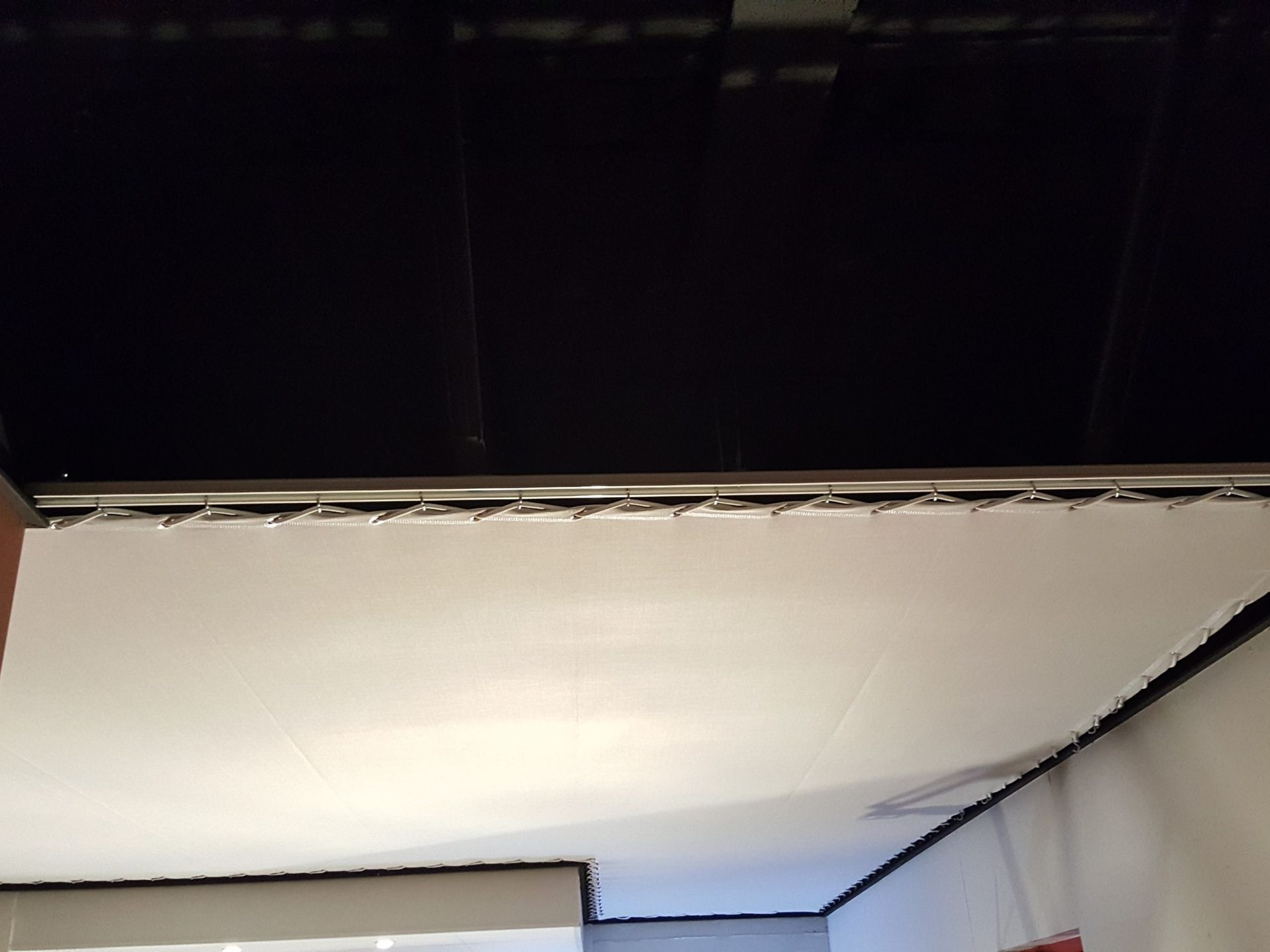 Un grand écran blanc est suspendu à un plafond noir dans une pièce aux murs blancs.