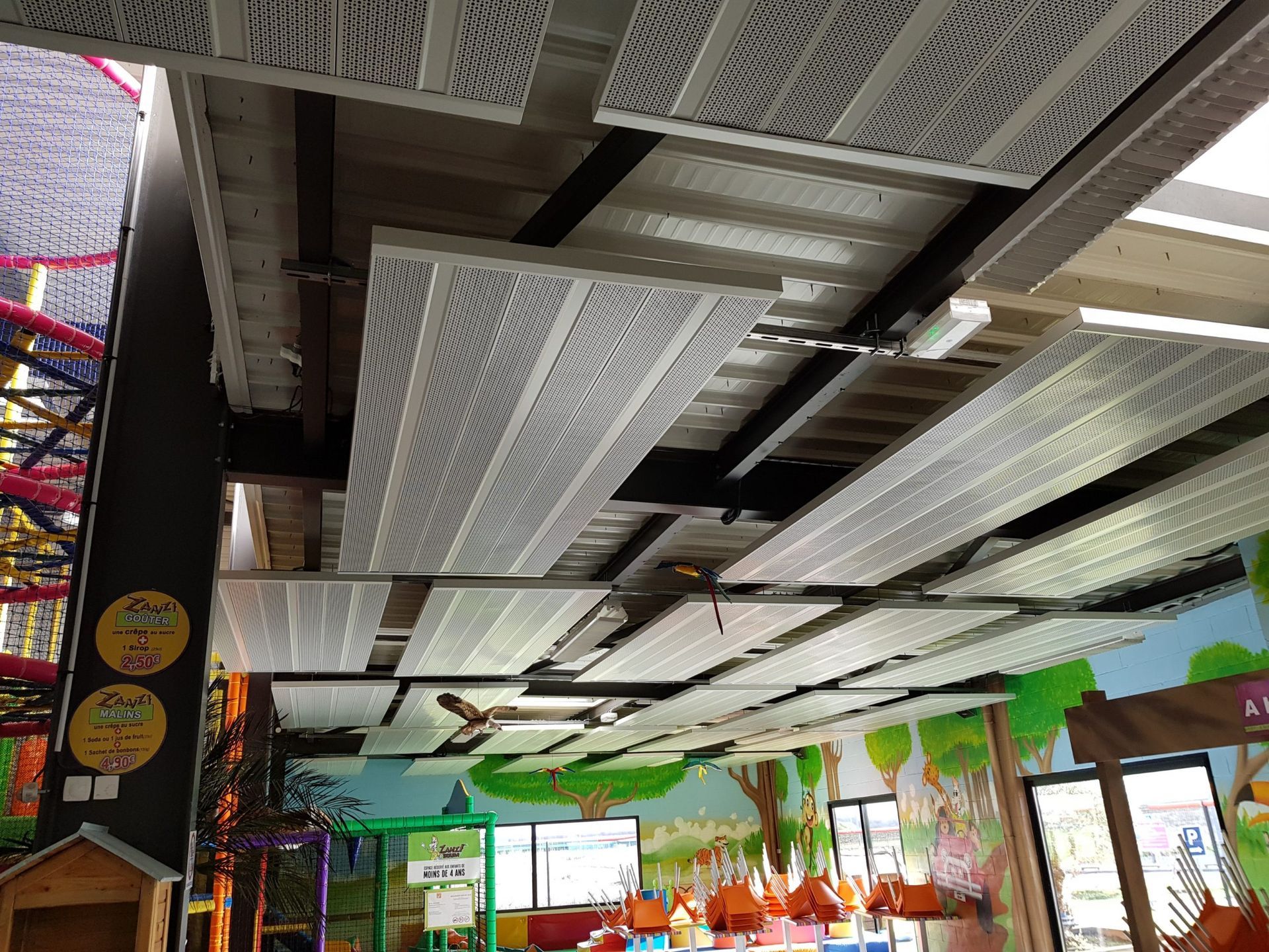 Vue intérieure d'une aire de jeux pour enfants avec des panneaux de plafond blancs et des décorations murales colorées.