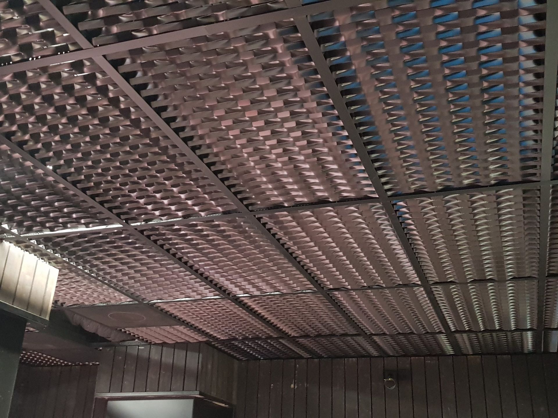 Plafond en grille métallique marron avec murs en bois.