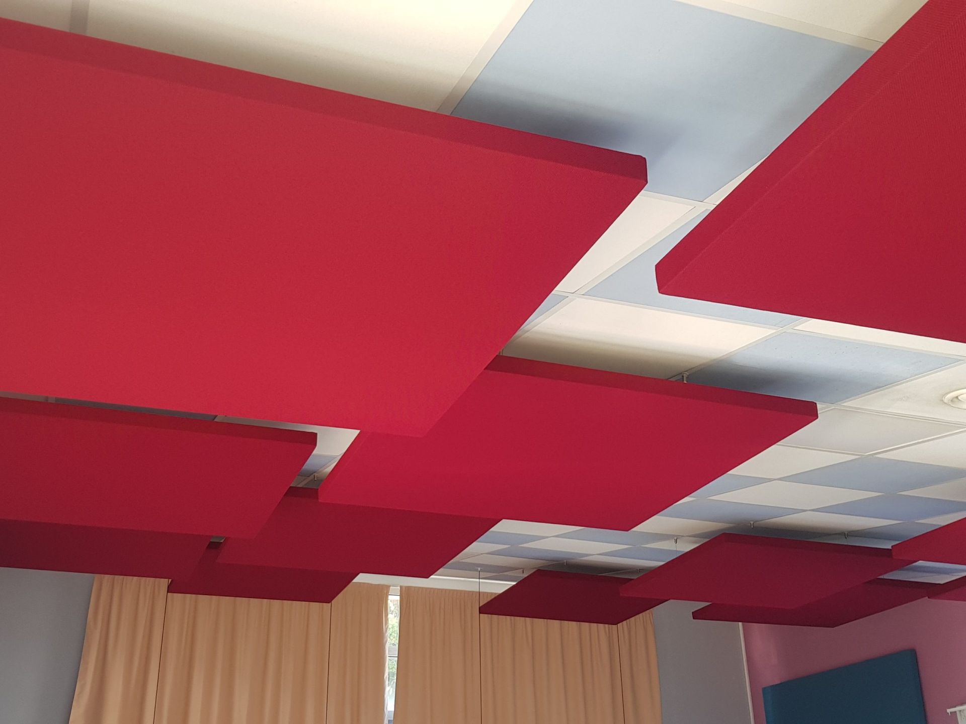 Panneaux acoustiques rouges installés sur un plafond à motifs blancs et bleus.