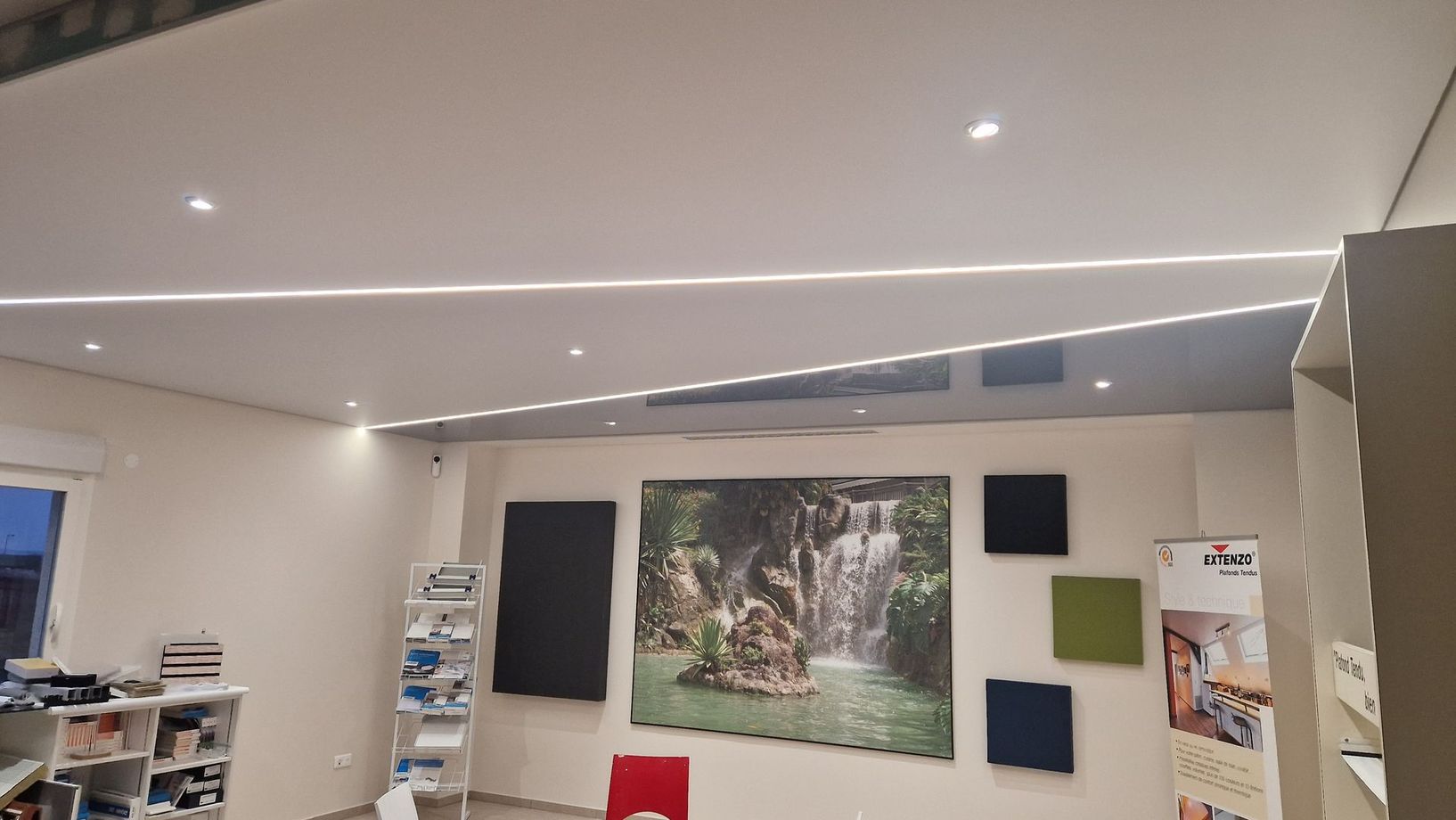 Intérieur d'une pièce avec panneaux acoustiques, une œuvre d'art en cascade et un éclairage encastré au plafond.