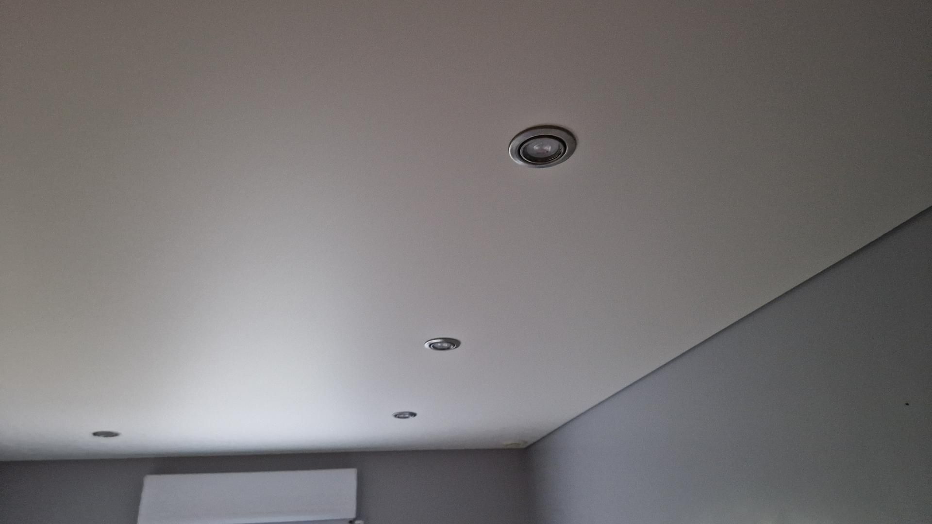 Plafond blanc avec trois spots encastrés, au-dessus d'un mur gris.