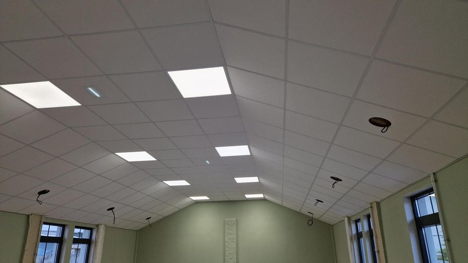 Plafond en carreaux blancs avec lumières carrées dans une pièce vert clair avec fenêtres.