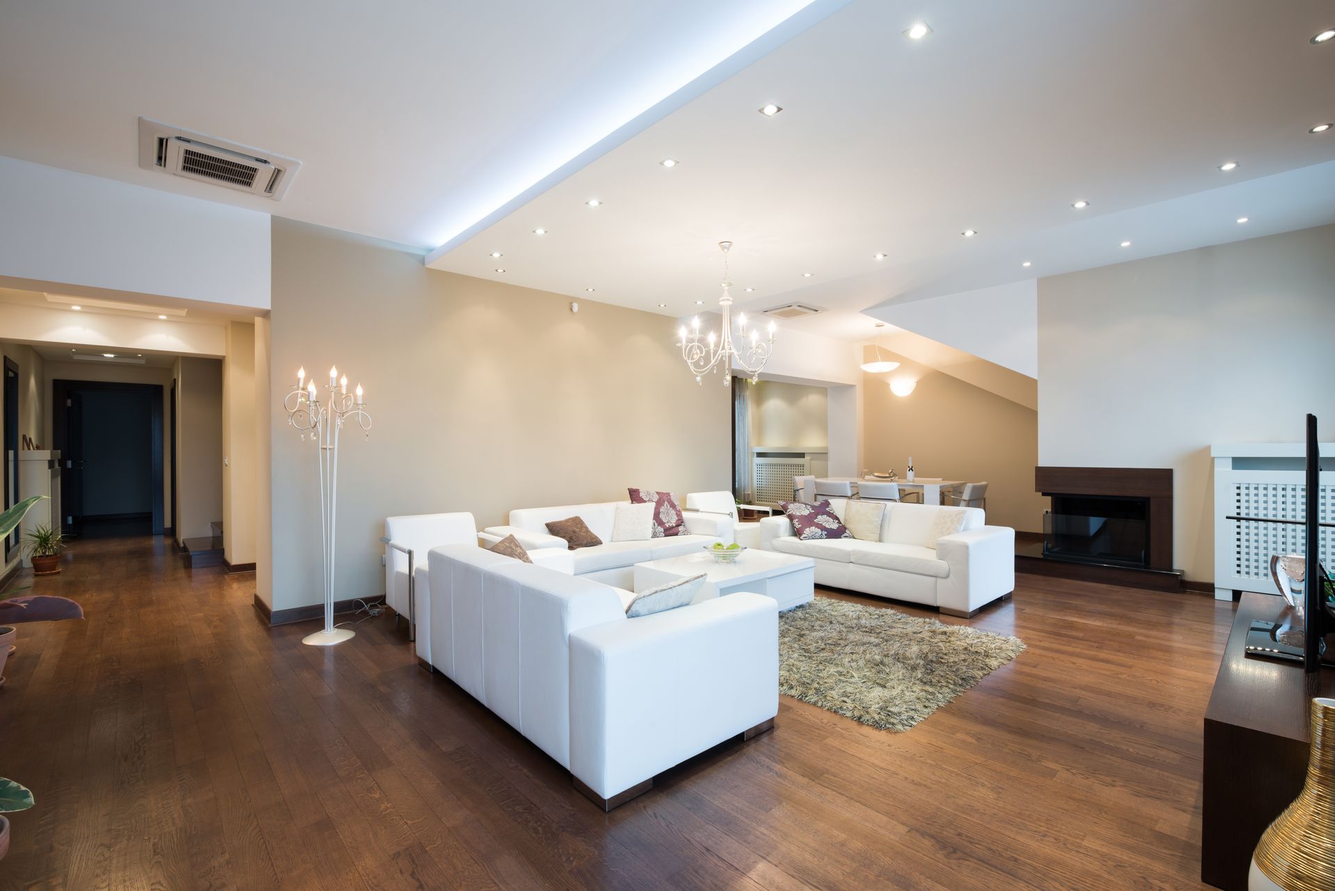 Salon spacieux avec canapés blancs, parquet et cheminée. Éclairage encastré.