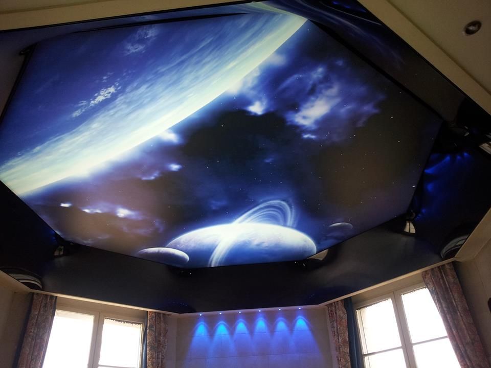 Plafond de la pièce avec une projection sur le thème de l'espace montrant des planètes, des nuages ​​et une partie d'une galaxie, avec un éclairage dans les tons bleus.