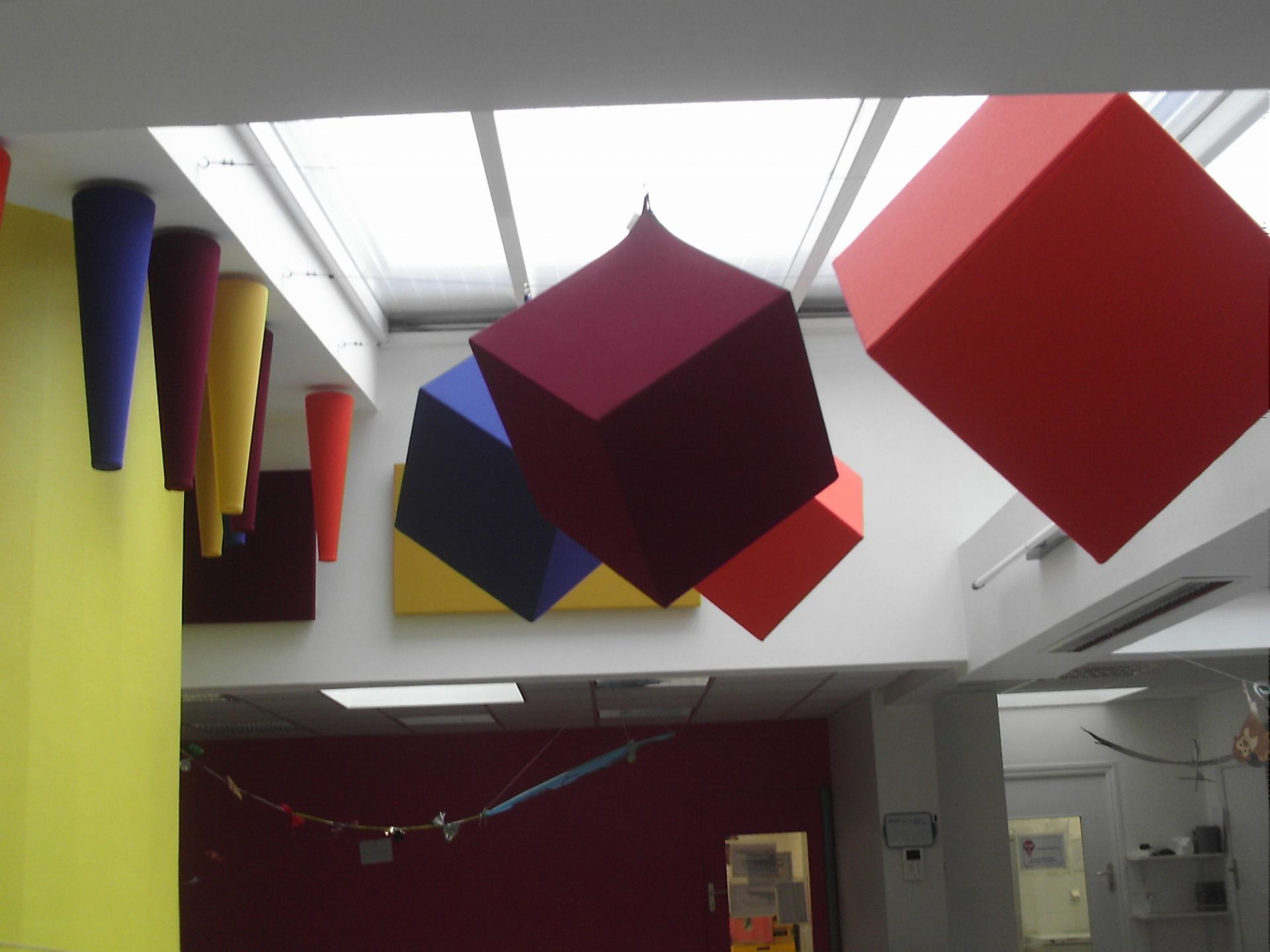 Formes géométriques colorées suspendues à un plafond blanc, notamment des cubes et des cônes.