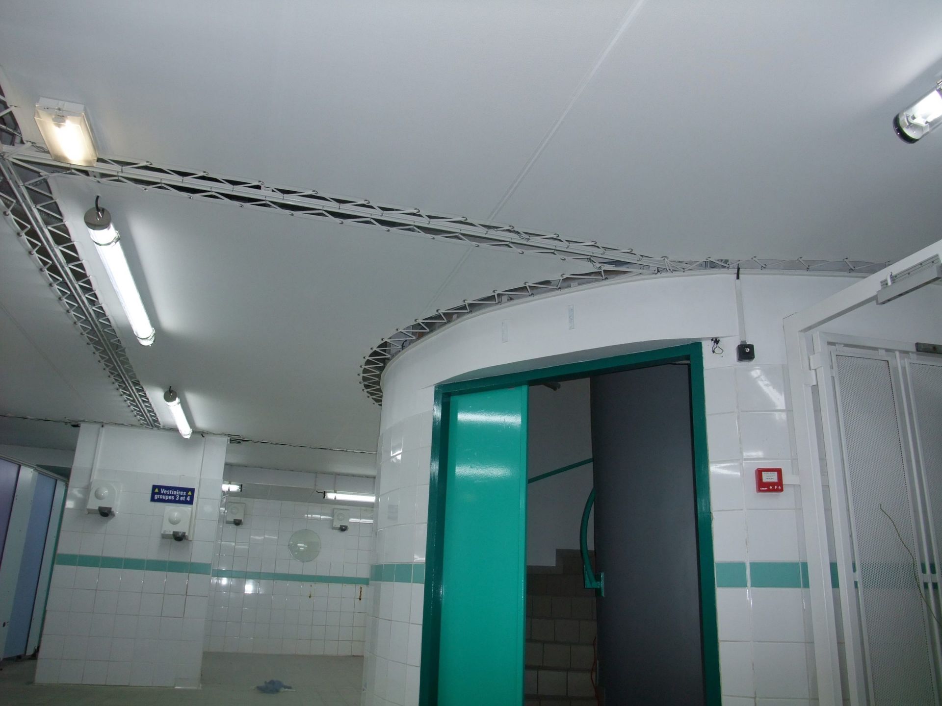 Intérieur d'une station de métro. Murs carrelés blancs, porte verte incurvée et éclairage fluorescent.