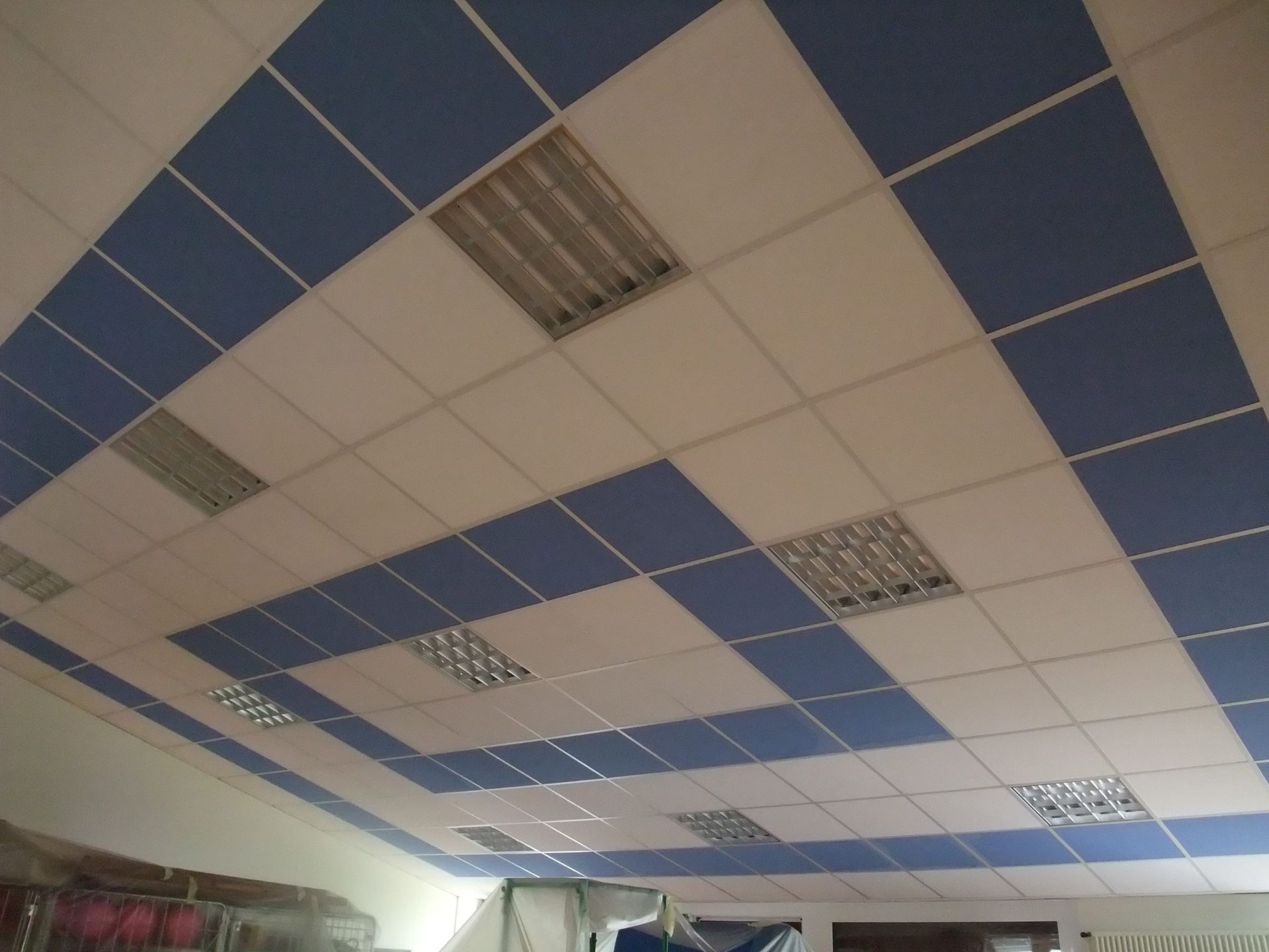 Plafond carrelé bleu et blanc avec lumières fluorescentes rectangulaires.