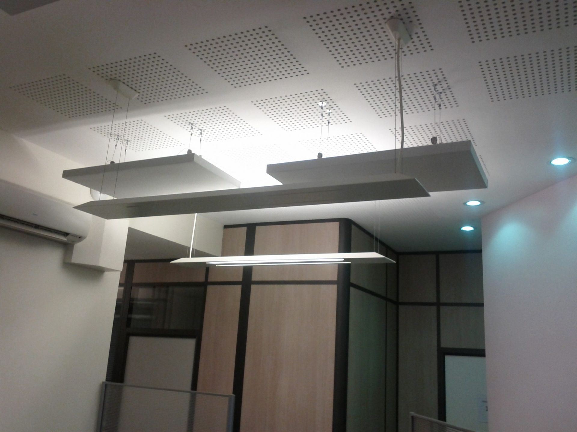 Plafond de bureau avec luminaires rectangulaires suspendus et panneaux acoustiques perforés.