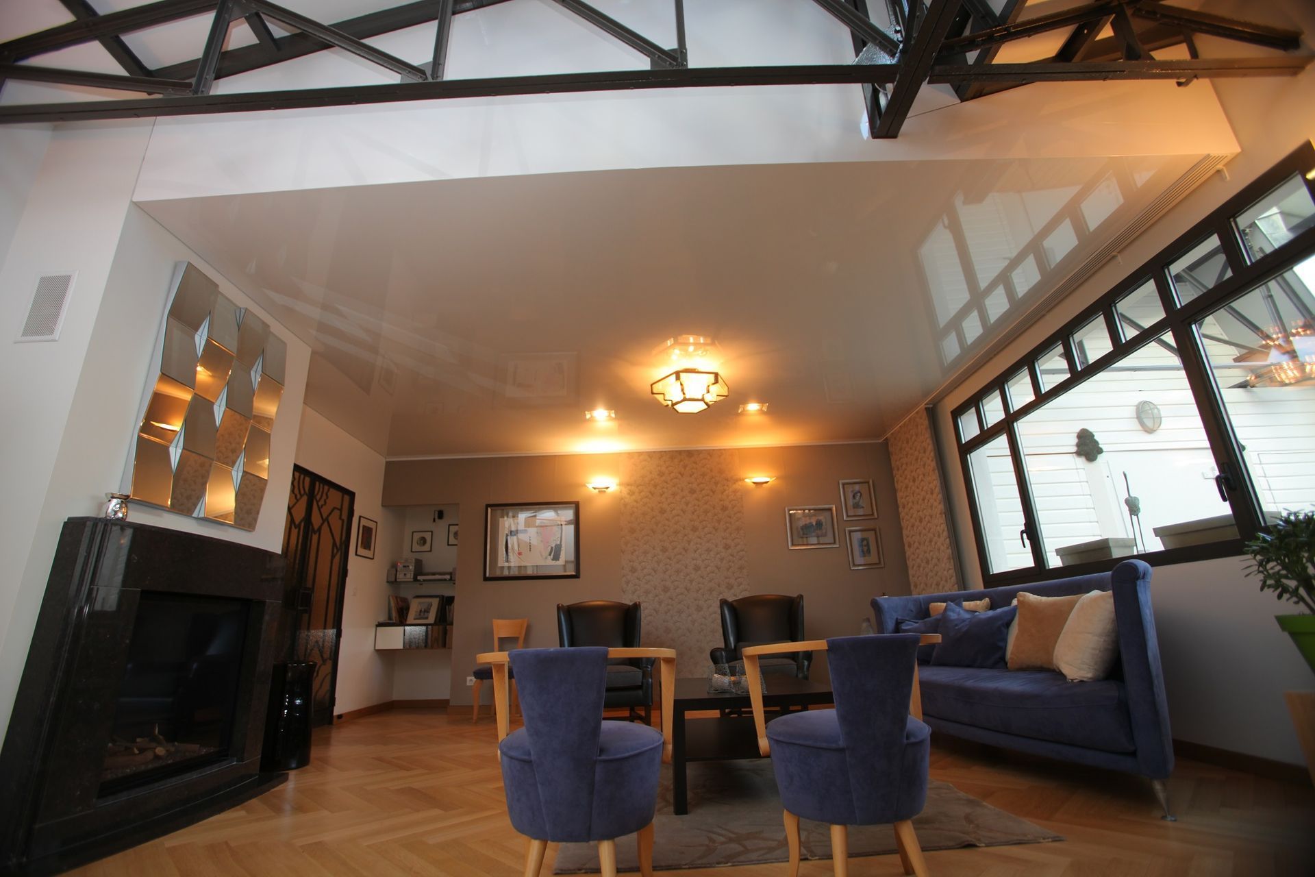 Salon avec cheminée, meubles bleus, grandes fenêtres et éclairage décoratif.