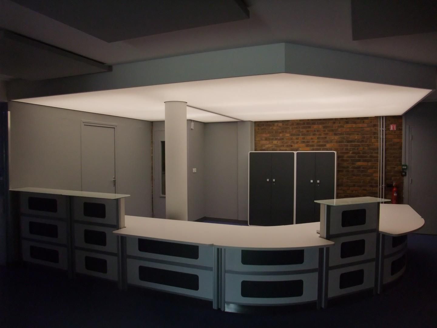 Comptoir de réception avec façade incurvée, armoires grises et plafond lumineux.