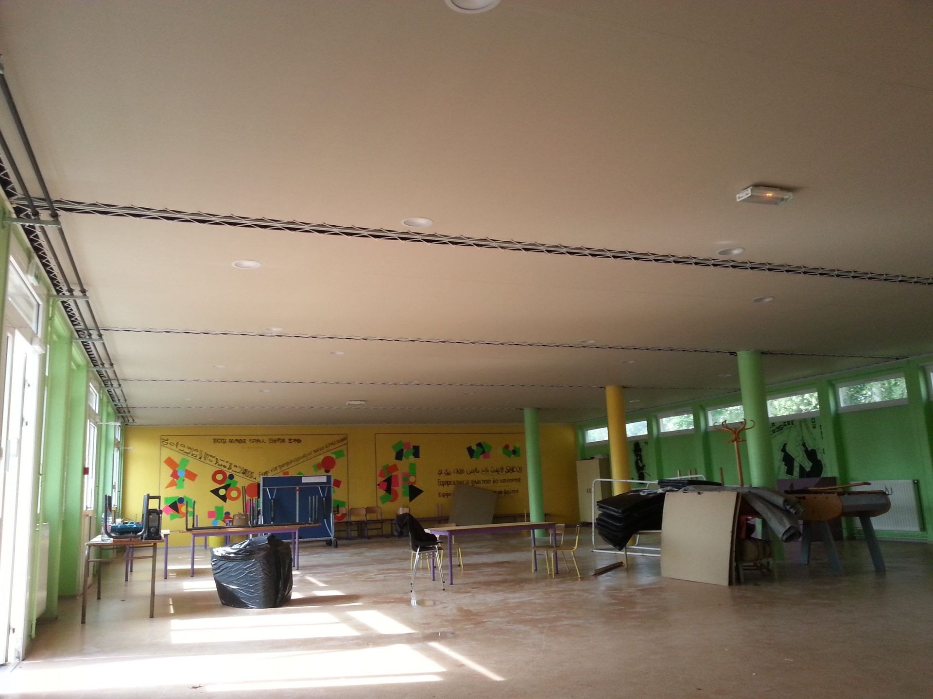 Chambre spacieuse avec un haut plafond, des tables et une fresque colorée sur le mur du fond.