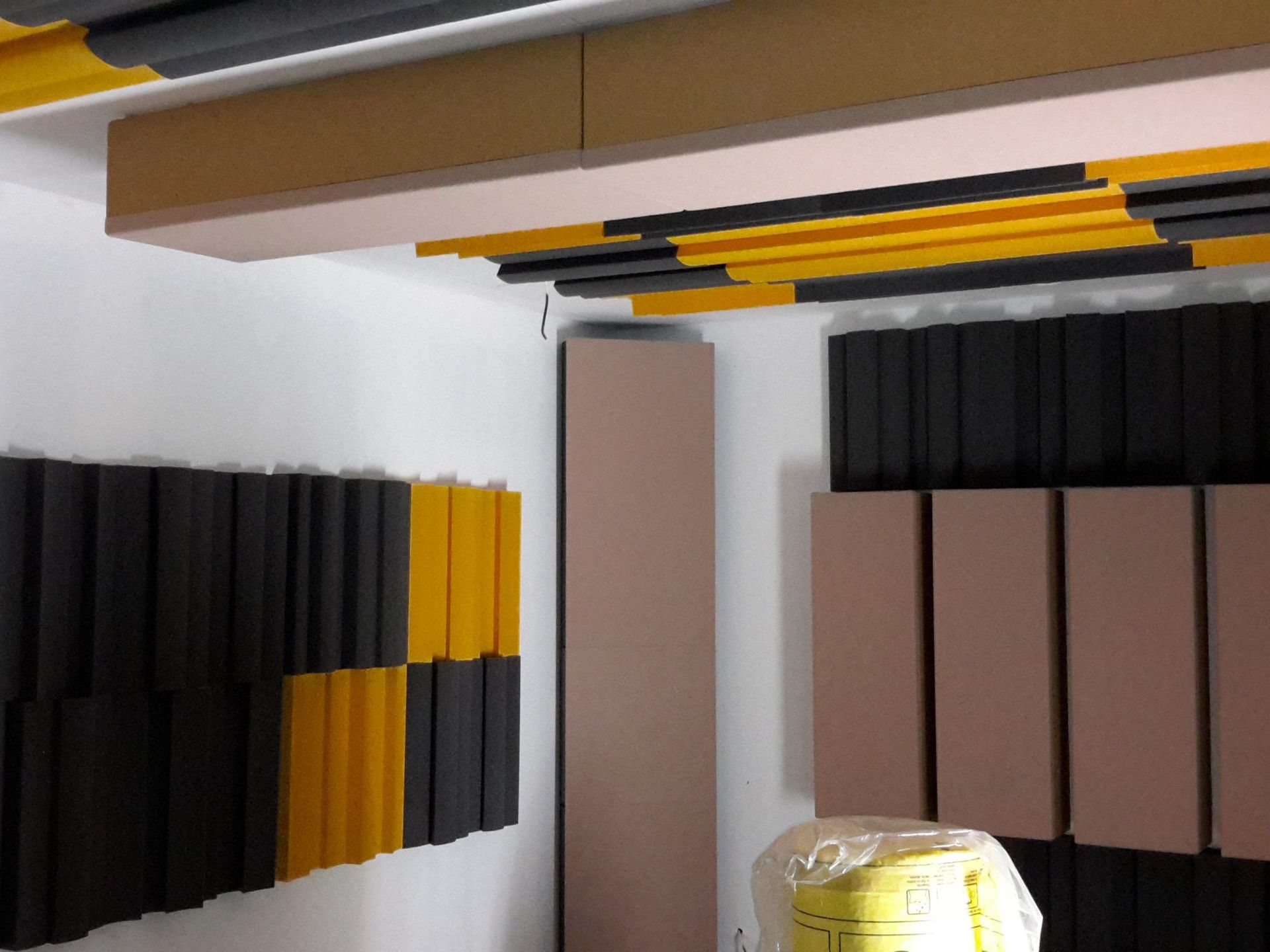 Panneaux acoustiques noirs et jaunes sur les murs et le plafond d'une pièce, probablement pour l'insonorisation.