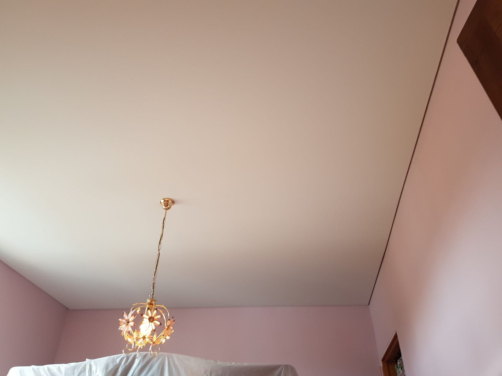 Plafond de pièce rose avec un lustre doré. Une ligne sombre longe le mur et l'angle du plafond.