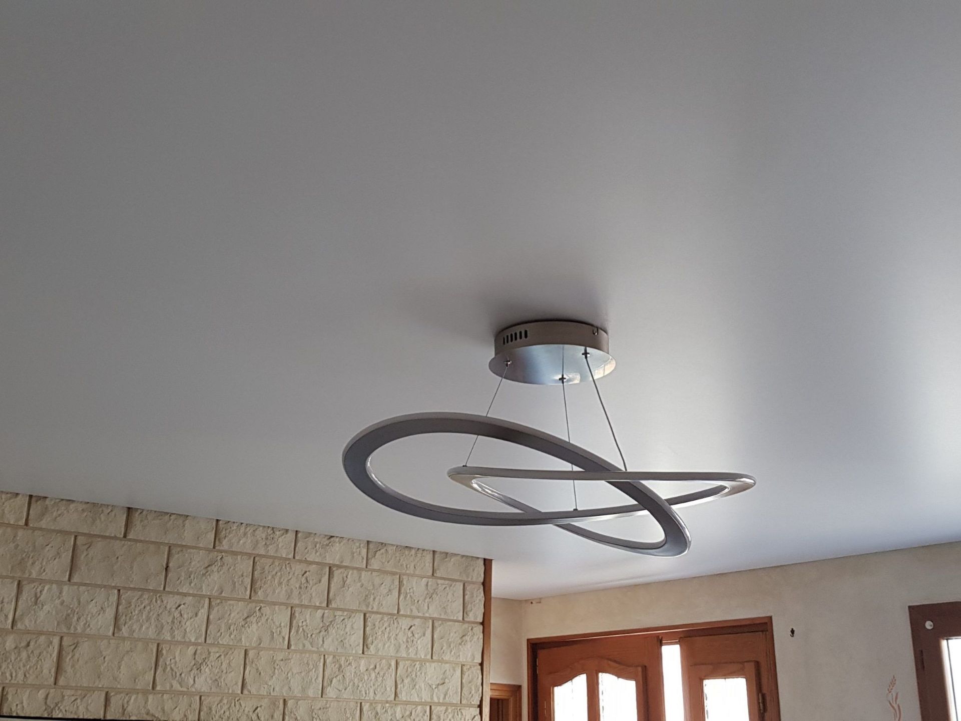 Un lustre moderne avec deux anneaux entrelacés est suspendu à un plafond blanc.
