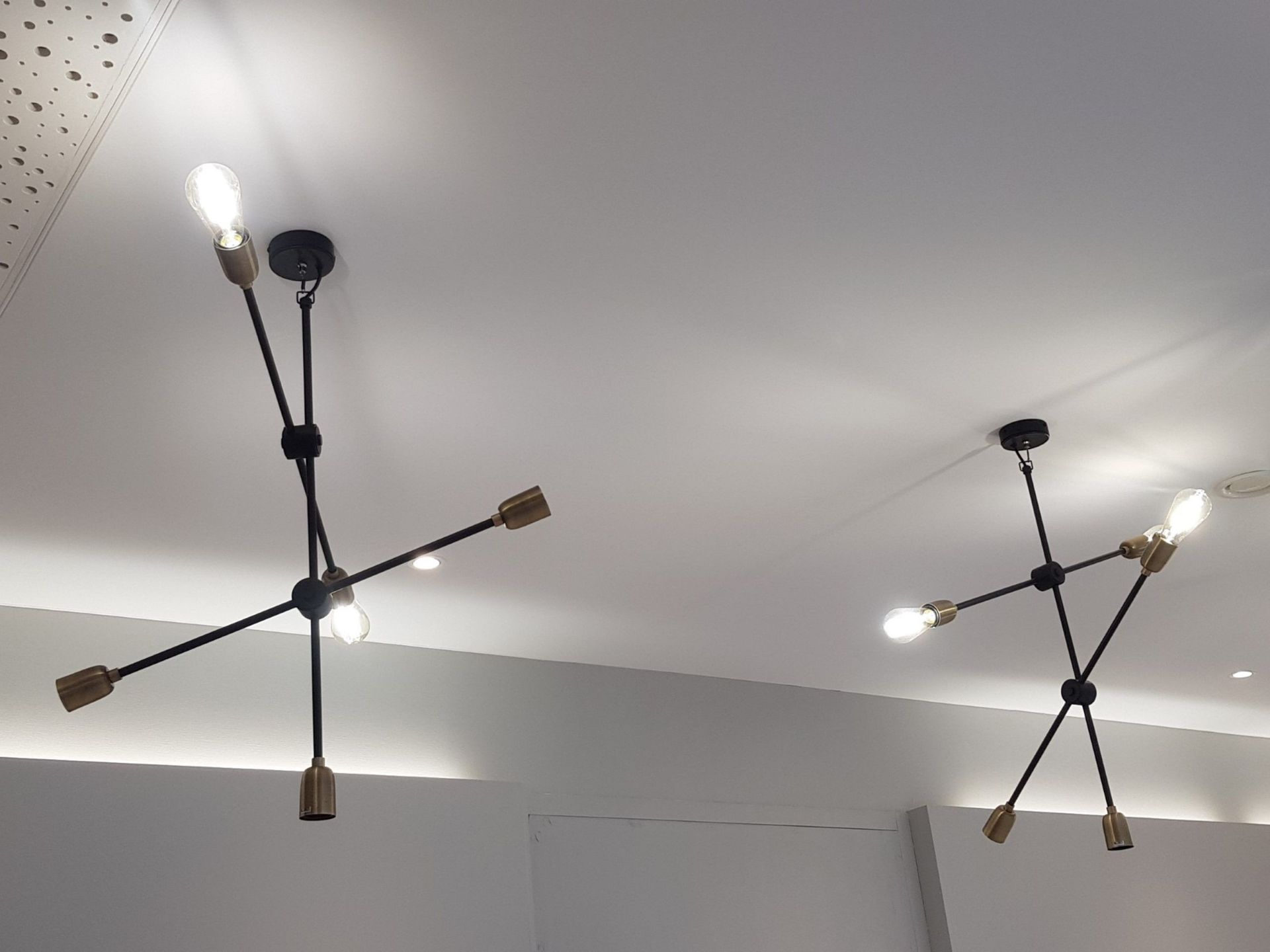 Deux lustres modernes noirs et dorés suspendus à un plafond blanc, chacun avec plusieurs bras et ampoules.