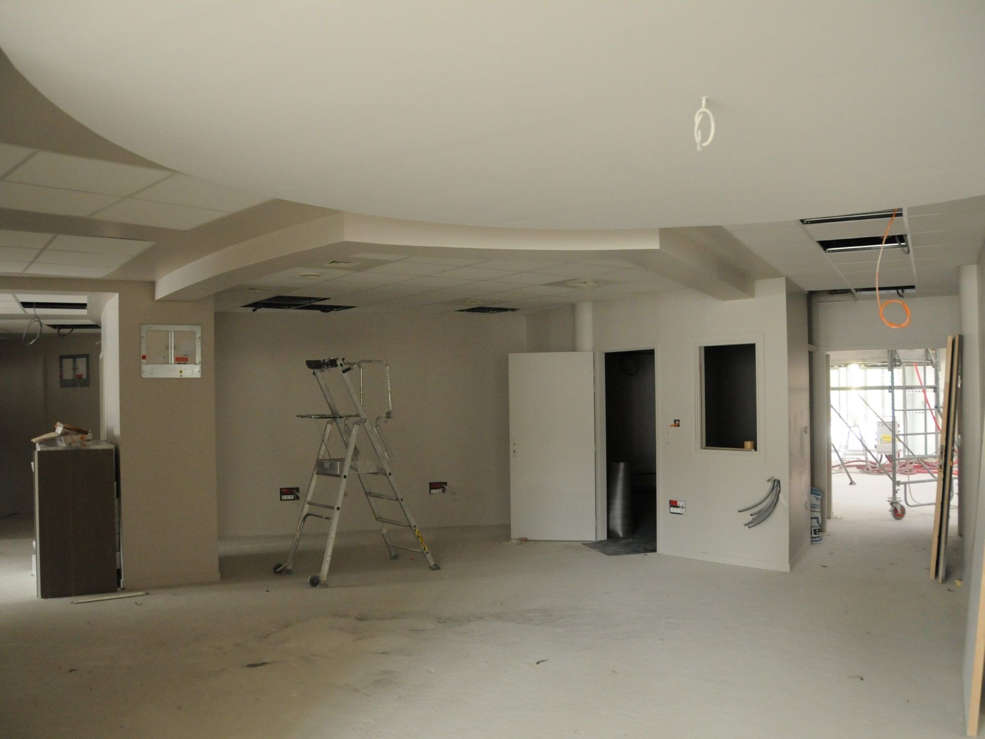 Intérieur d'une pièce en construction avec murs, plafond et sol en béton non finis ; un escabeau est présent.