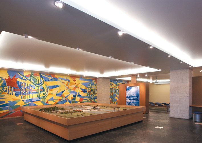 Vue intérieure d'une pièce avec une grande maquette en bois, une fresque murale colorée et un éclairage encastré.