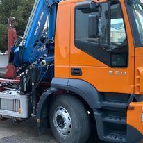 Un camión naranja con una grúa azul en la parte trasera está estacionado al costado de la carretera.