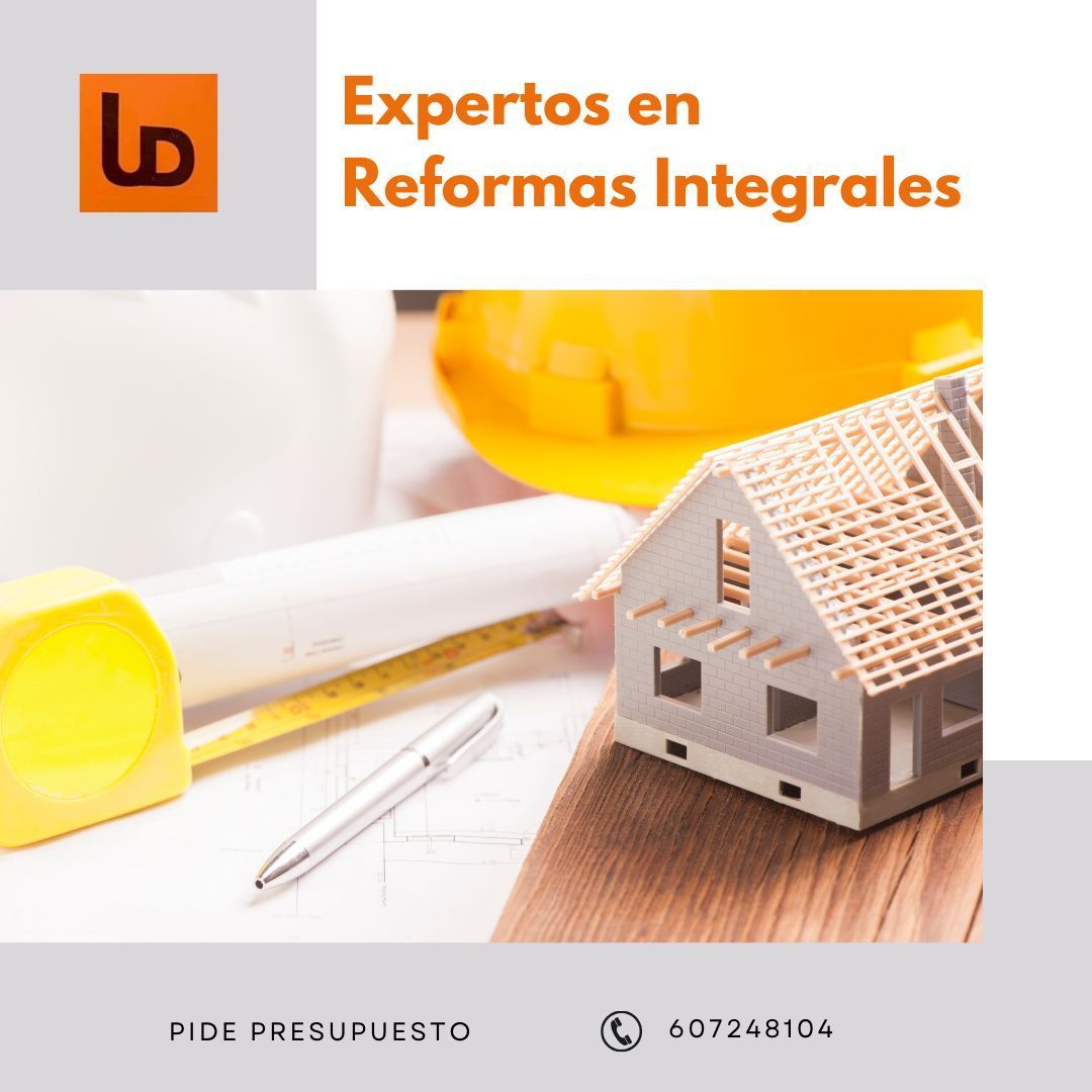 Una casa modelo está sobre una mesa de madera al lado de un casco y un bolígrafo.