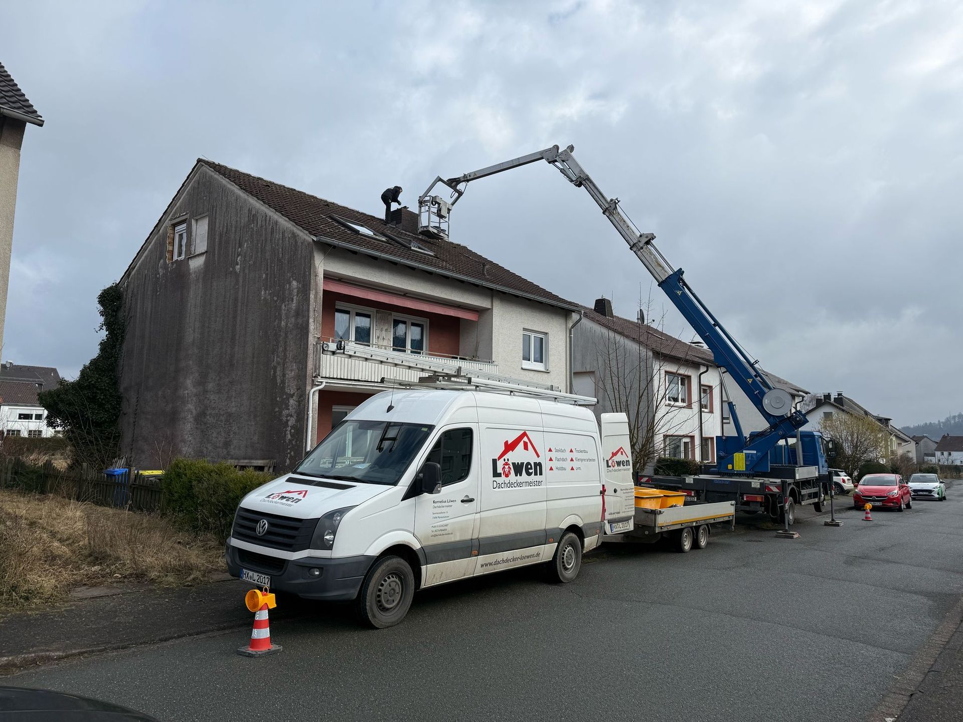 Vor einem Gebäude parkt ein weißer Lieferwagen, an dem ein Kran befestigt ist.