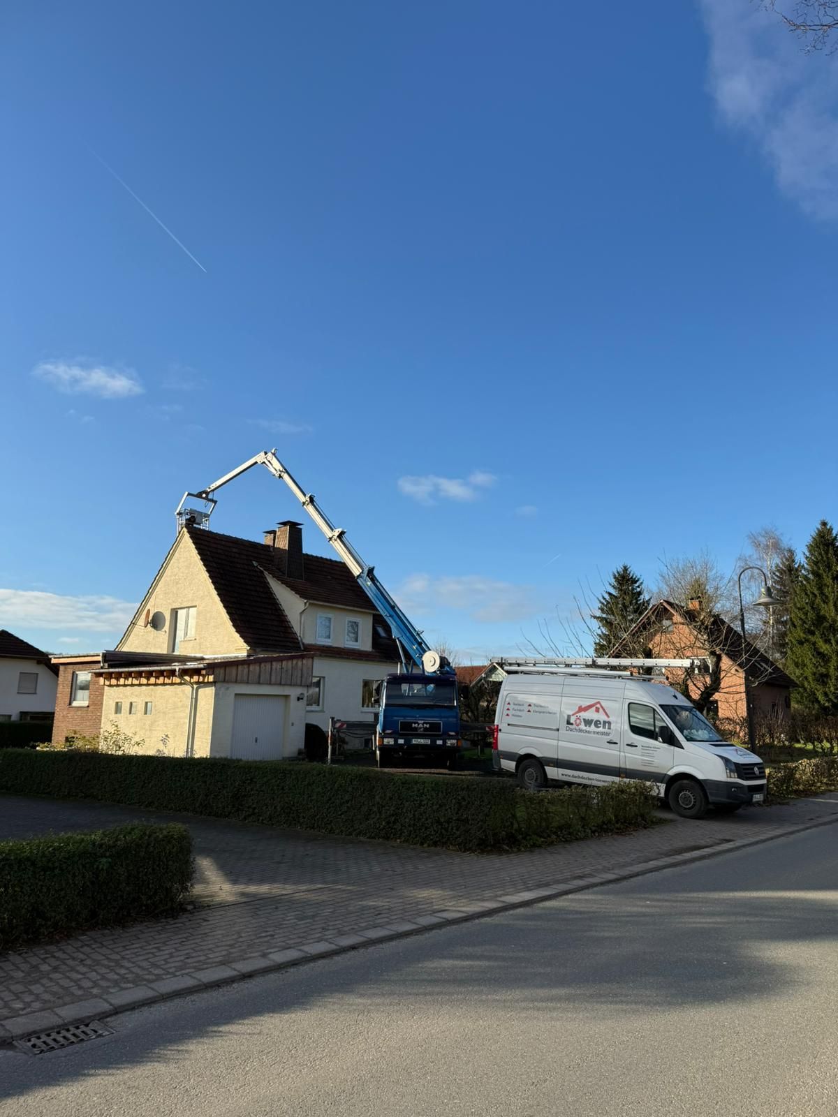 Vor einem Haus parkt ein weißer Lieferwagen mit einem Kran auf dem Dach.