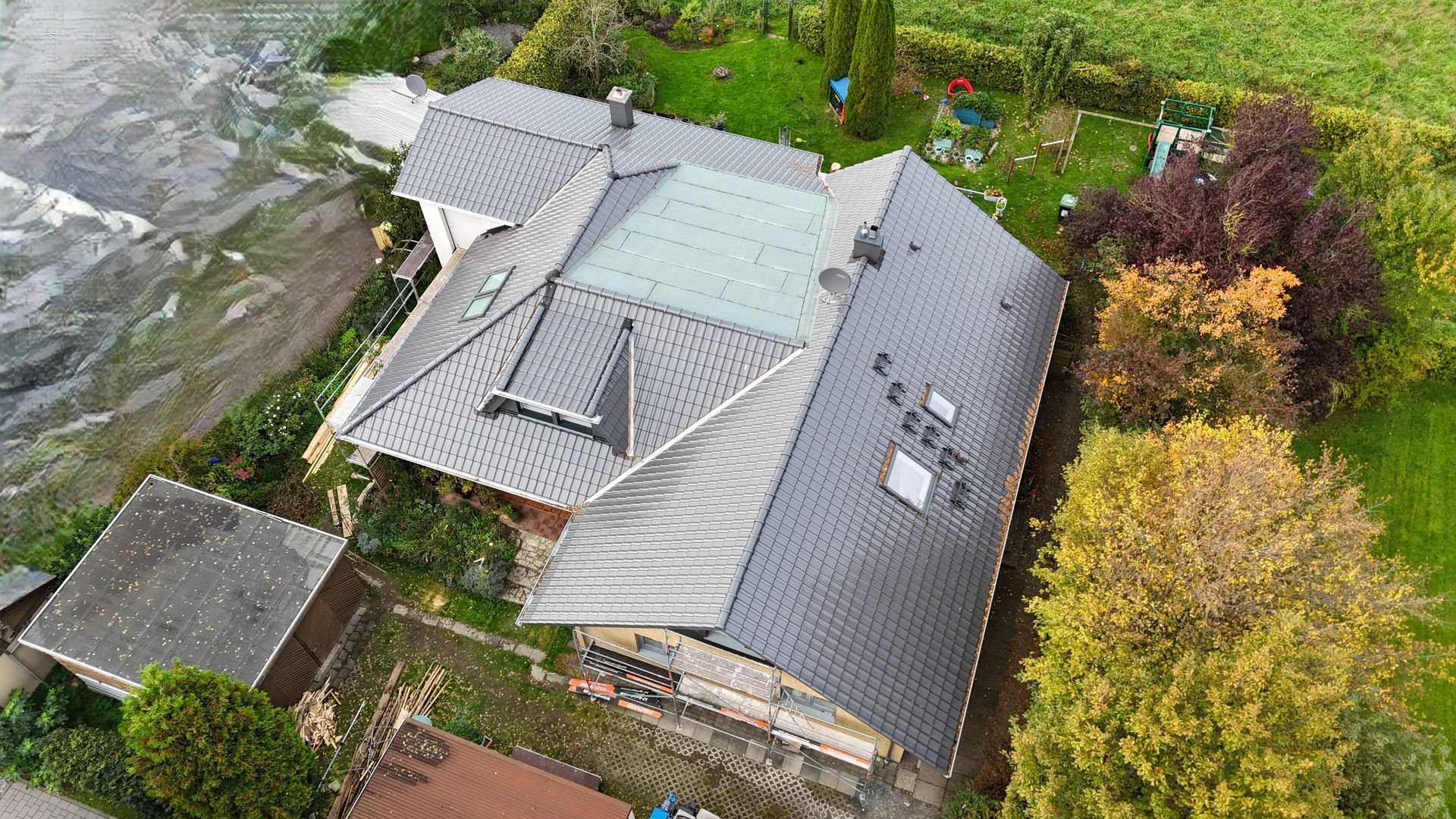 Eine Luftaufnahme eines Hauses mit einem Dach, das von Bäumen und Gras umgeben ist.