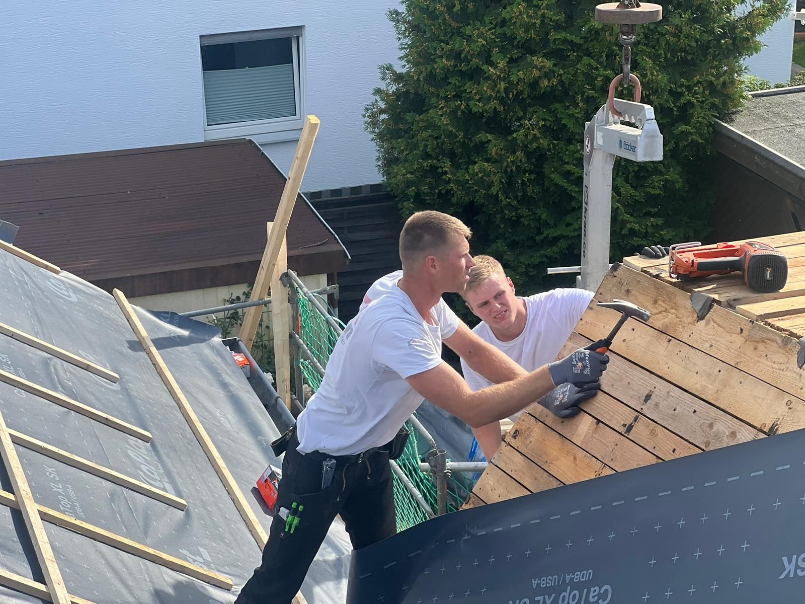 Zwei Männer arbeiten mit einem Hammer auf einem Dach.