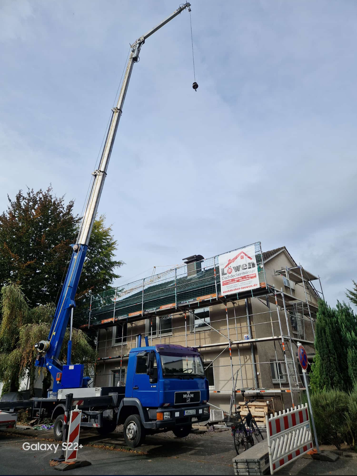 Ein blauer Lastwagen mit einem daran befestigten Kran steht vor einem im Bau befindlichen Gebäude.