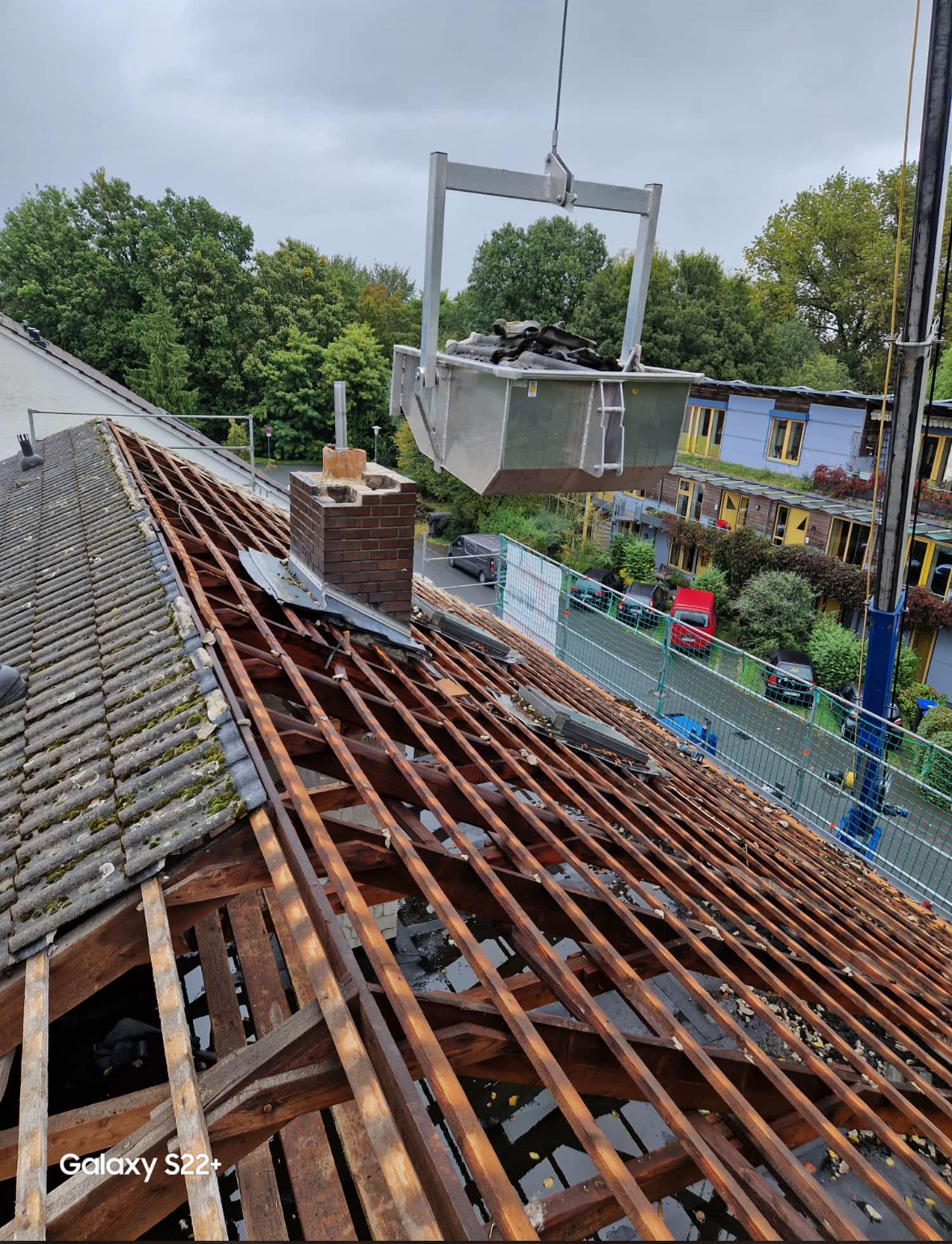 Ein Kran hebt einen Eimer über ein Dach.