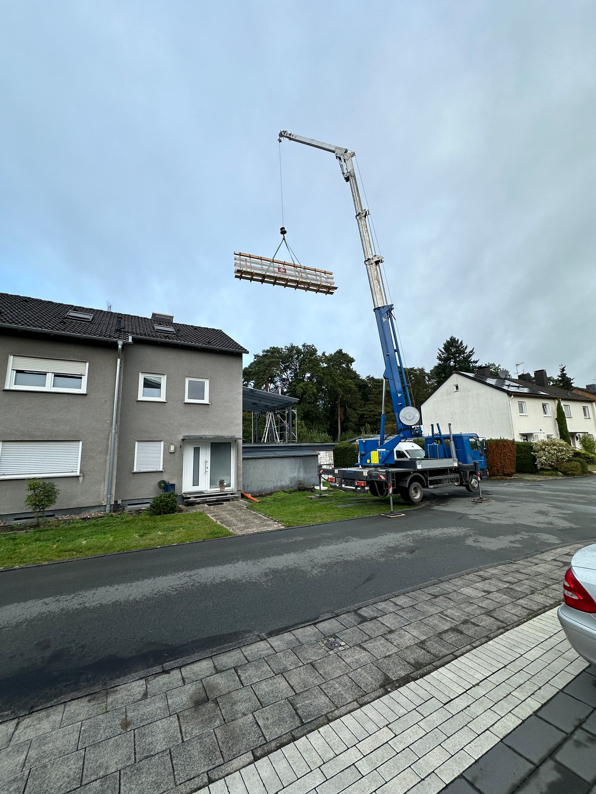 Ein Kran hebt ein Stück Holz über ein Haus.
