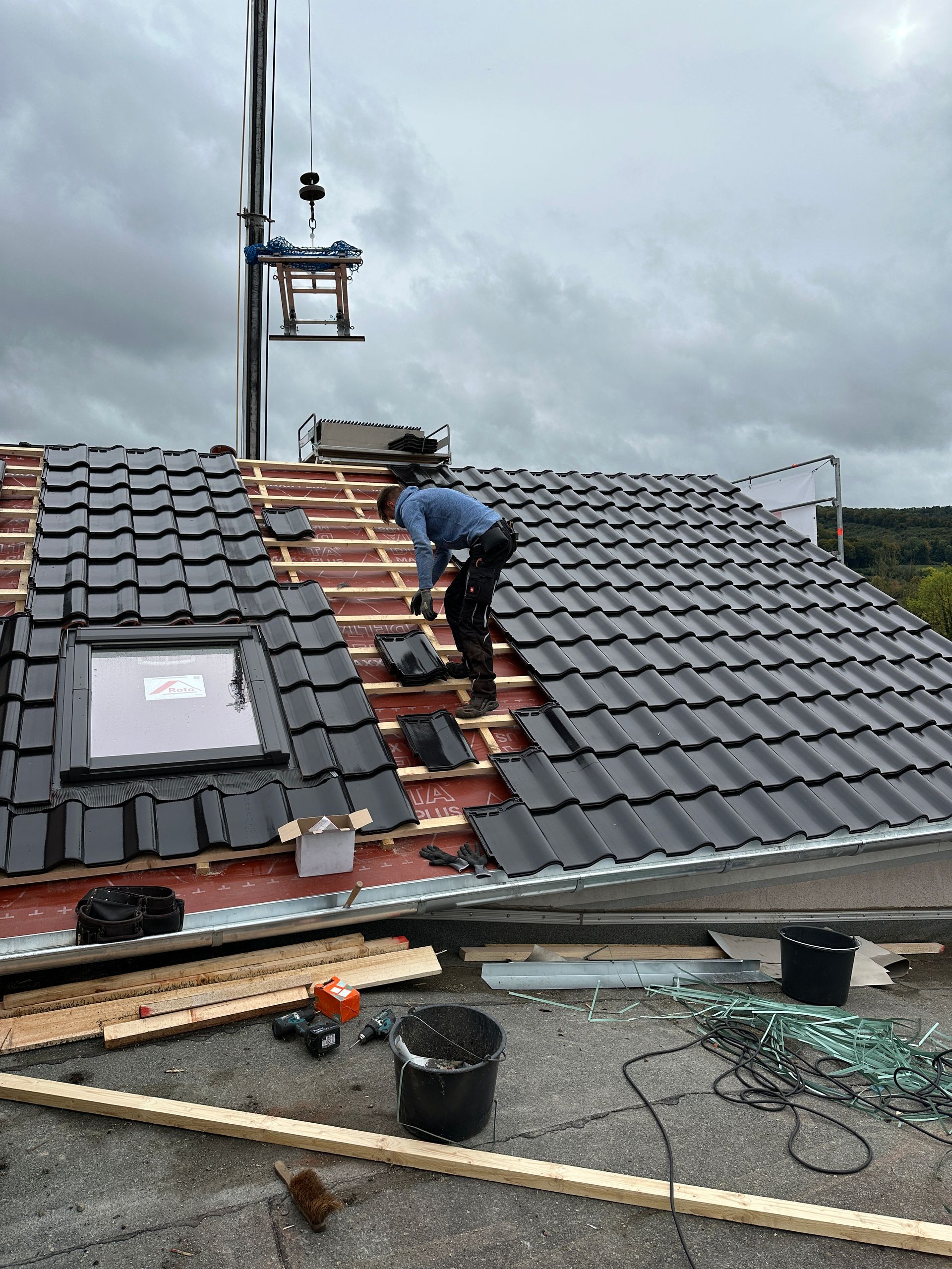 Ein Mann arbeitet auf einem Dach, im Hintergrund ist ein Kran zu sehen.