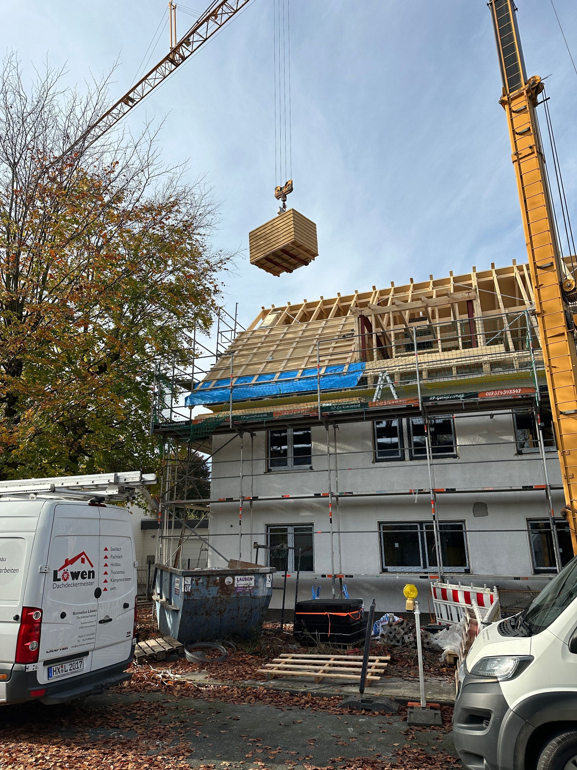 Ein Kran hebt eine Holzkiste über ein im Bau befindliches Gebäude.