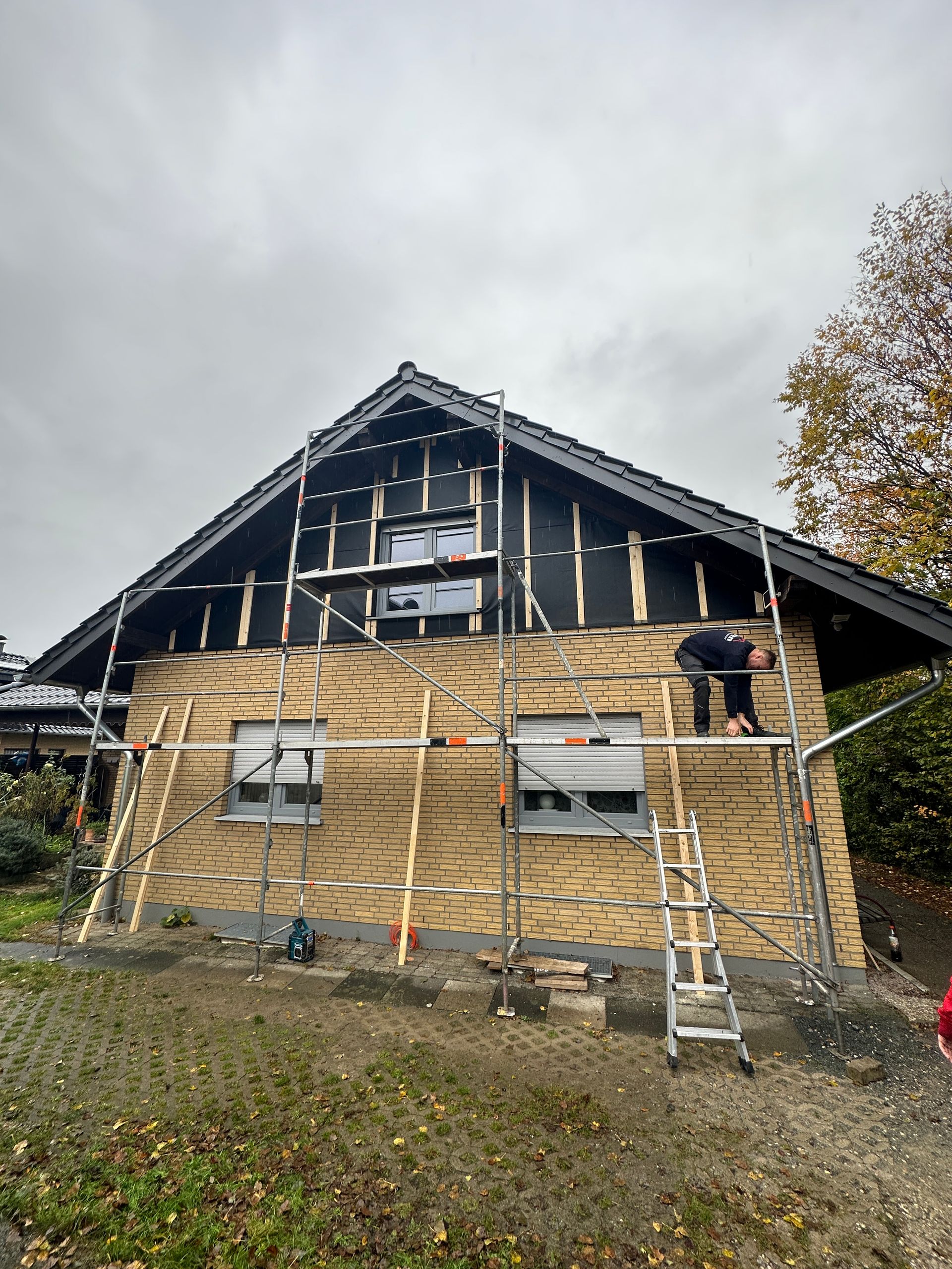 Ein Mann steht auf einem Gerüst an der Seite eines Hauses.