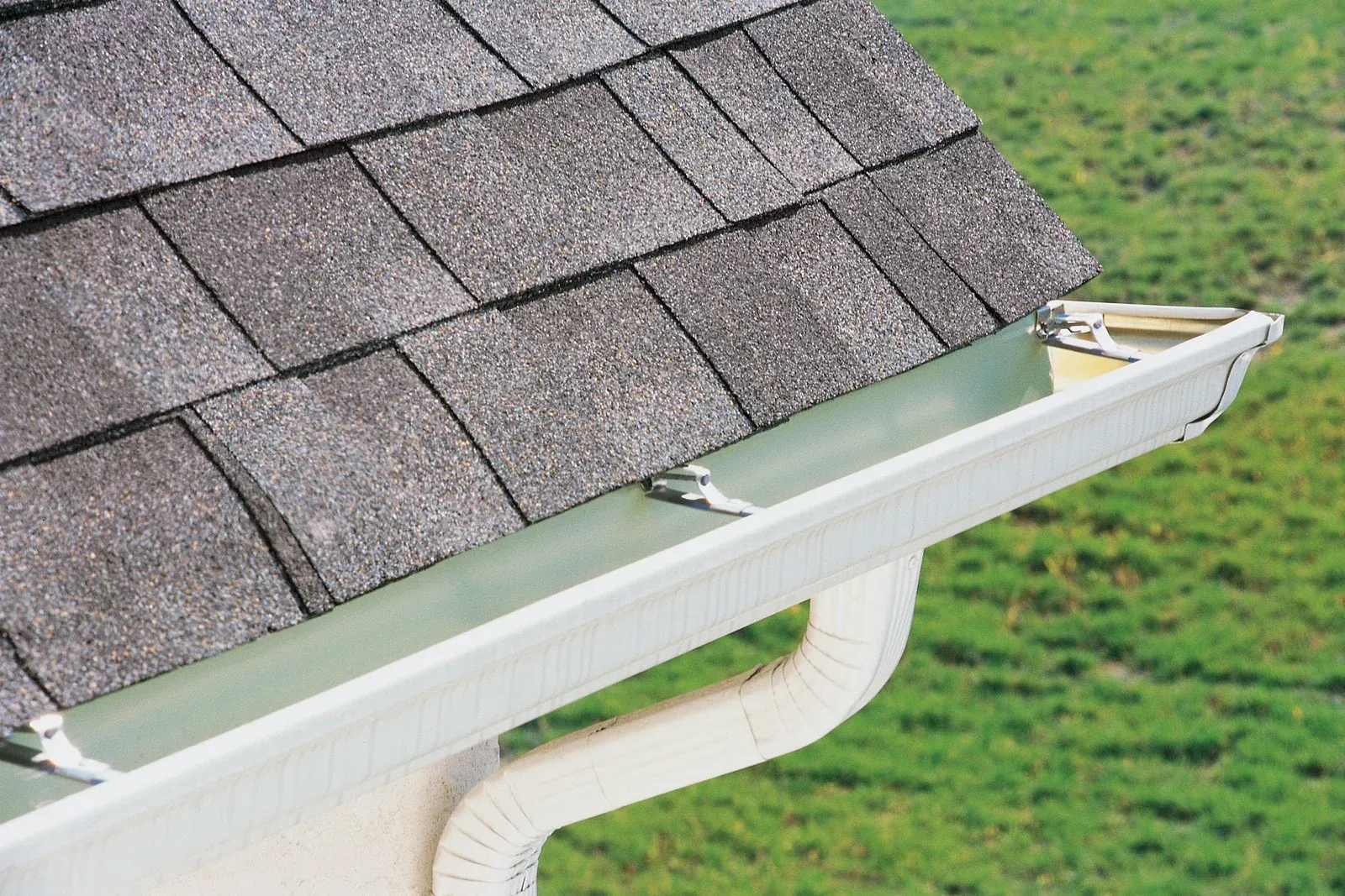 House roof with gray shingles and a white gutter on a green lawn background