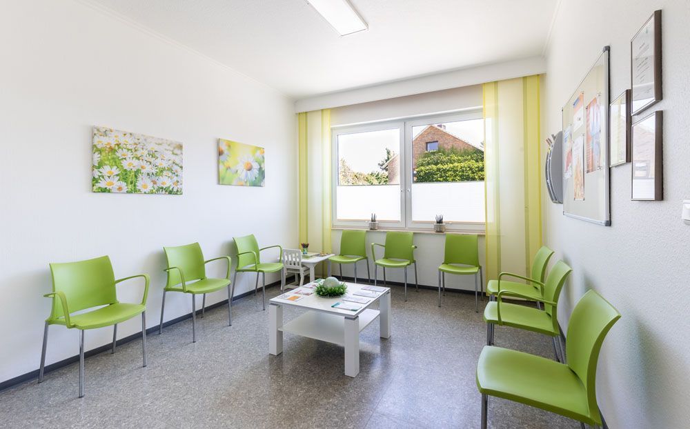 Ein Wartezimmer mit grünen Stühlen und einem weißen Tisch