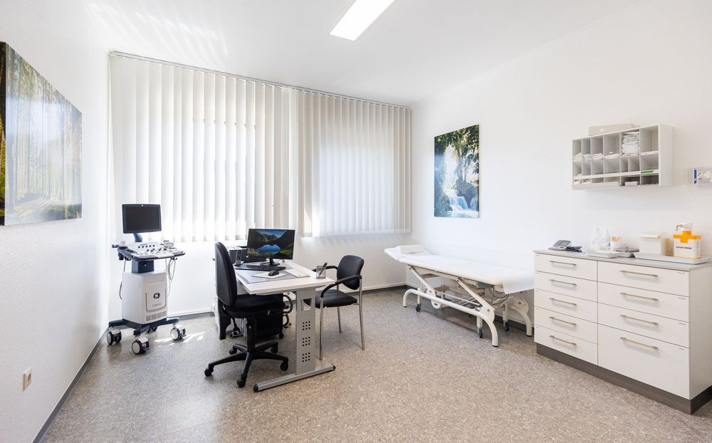 Eine Arztpraxis mit Schreibtisch, Stuhl, Computer und Bett.