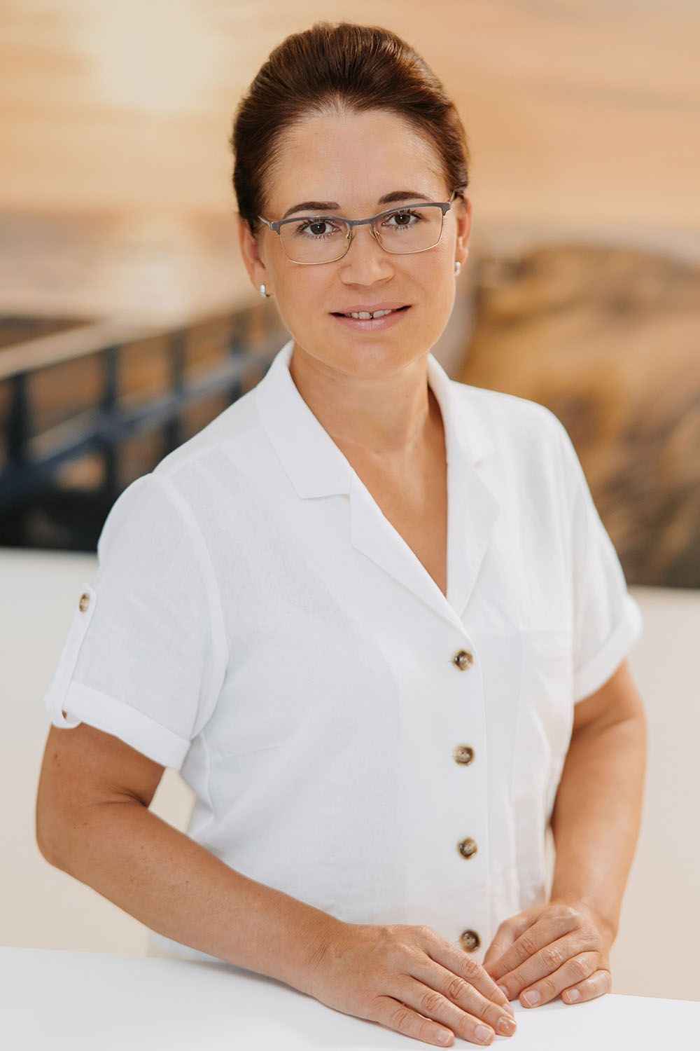 Eine Frau mit Brille und weißem Hemd steht neben einem Tisch.
