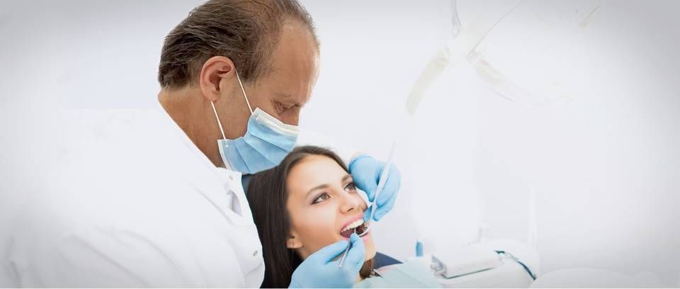 Ein Zahnarzt untersucht den Mund eines Patienten in einer hellen, klinischen Umgebung.