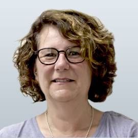 Frau mit langem, gewelltem braunem Haar, lächelnd vor neutralem Hintergrund.