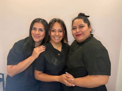 Tres personas con camisas oscuras sonriendo y posando juntas contra una pared lisa.