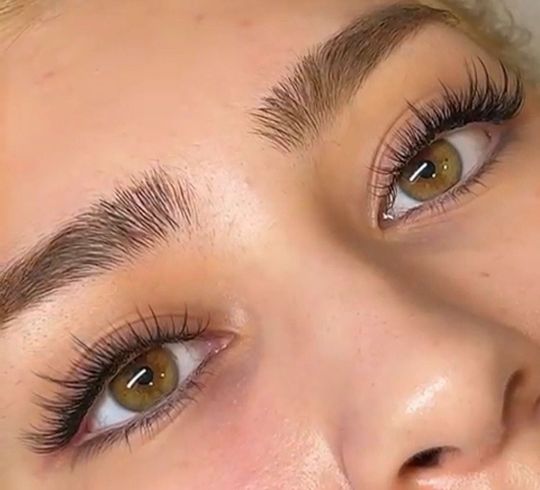 Primer plano de ojos marrones con largas pestañas rizadas y cejas bien definidas sobre un fondo de tono piel suave.
