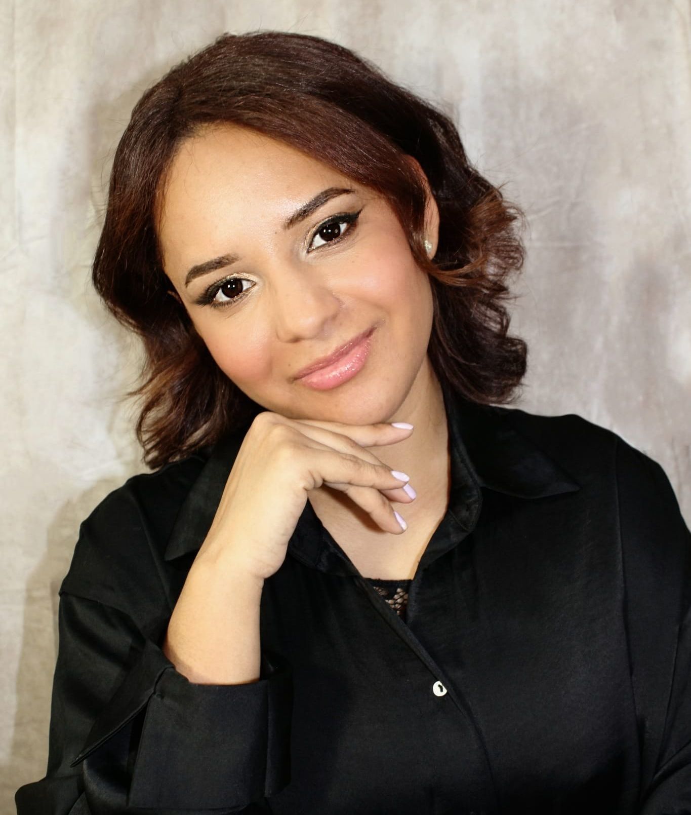 Una mujer con una camisa negra y la mano en la barbilla.