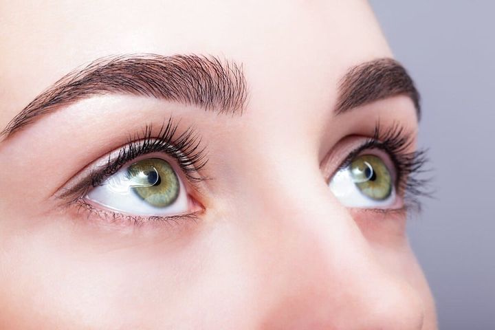 Primer plano de ojos verdes con cejas oscuras mirando hacia arriba.