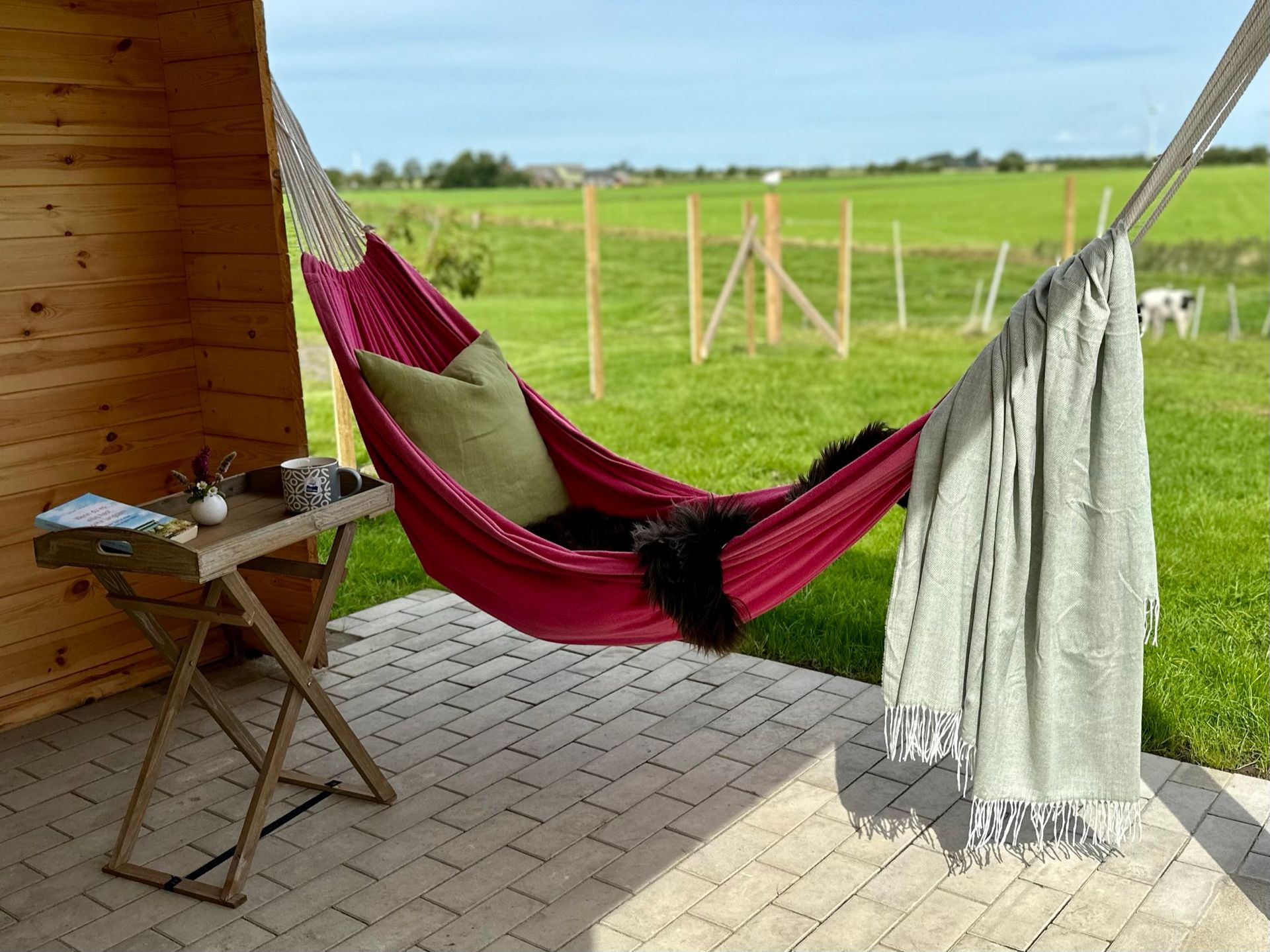Gemütliche Hängematte mit Kissen und Decke auf einer überdachten Terrasse mit Blick auf grüne Wiesen – perfekte Ruheoase im Ferienhaus an der Nordsee.